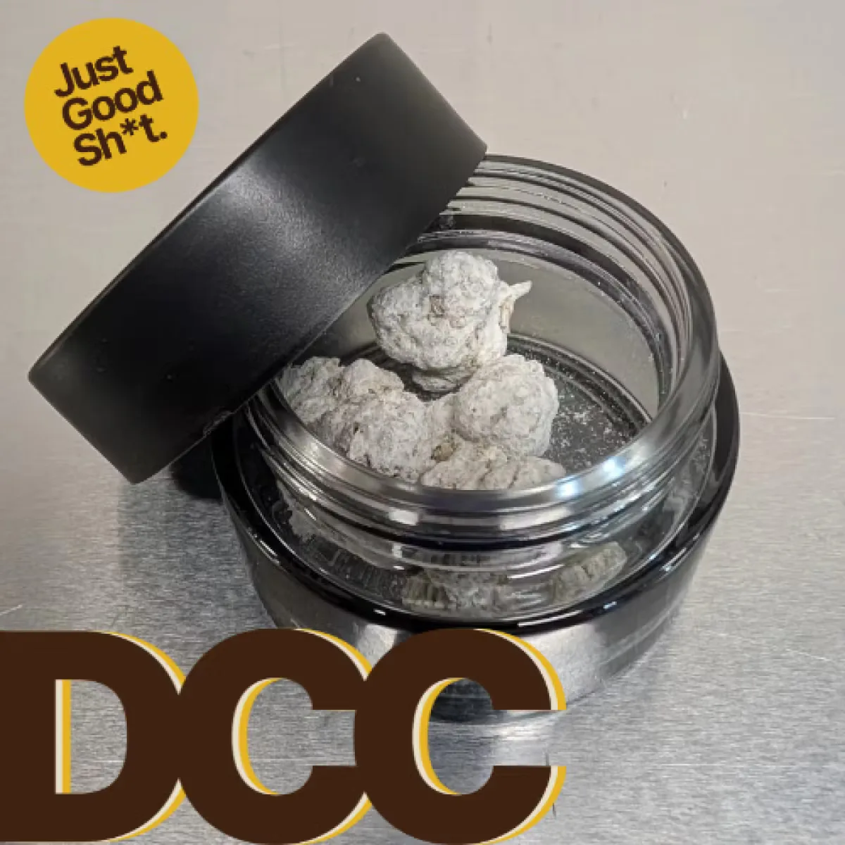 Open black-lidded glass jar of frosted, concentrate-coated cannabis buds, with the DCC logo and a yellow badge.