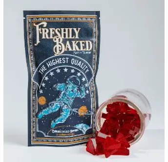 Navy Freshly Baked pouch with an astronaut illustration, beside a tipped glass jar of red gem-shaped gummies.