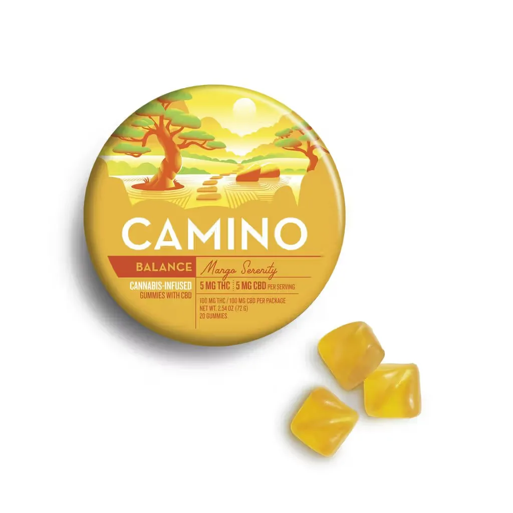Round yellow KIVA Camino tin with a tree and landscape scene, labeled mango, next to three yellow square gummies.