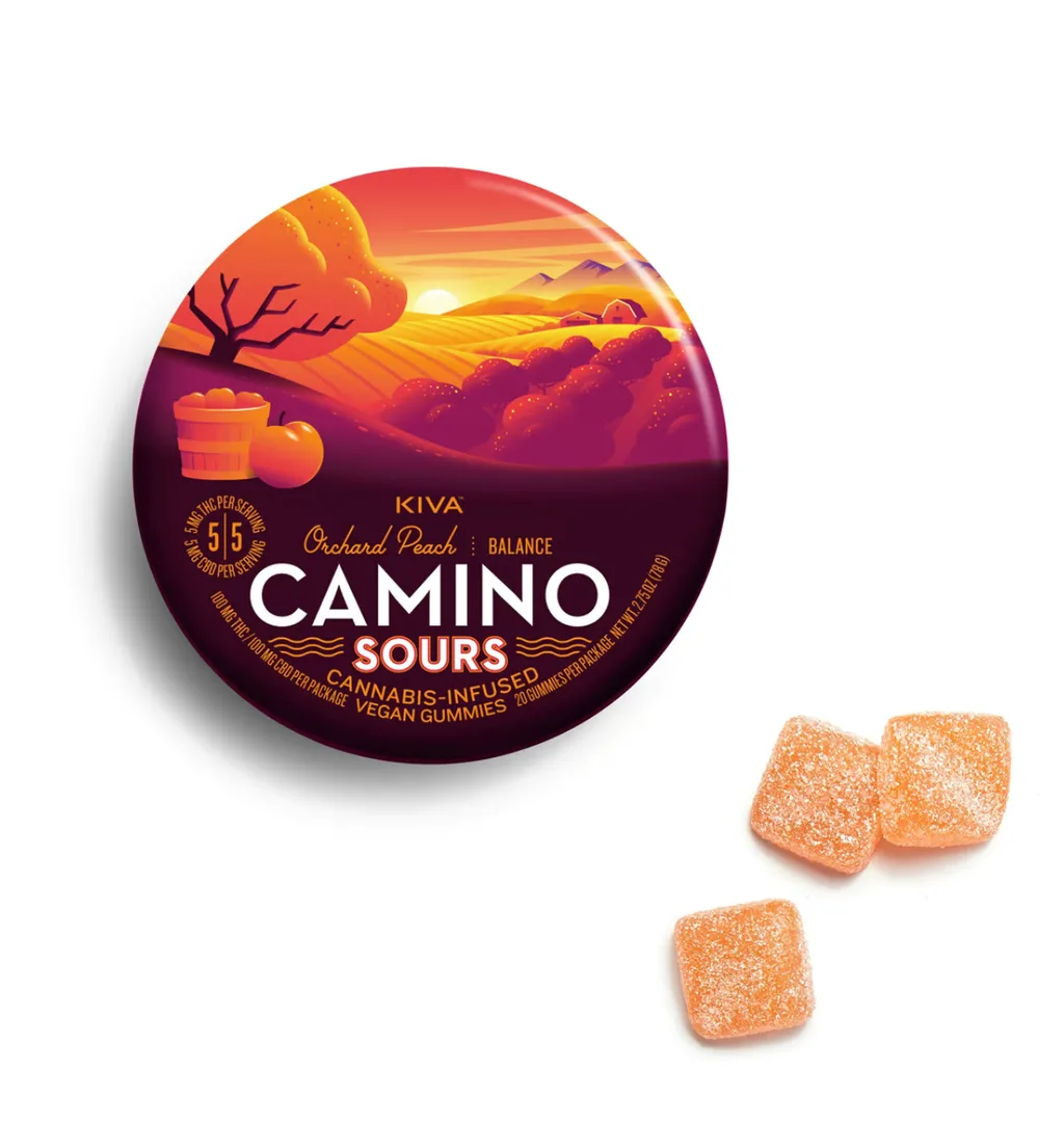 Round orange and purple KIVA Camino Sours Orchard Peach tin with a sunset orchard scene, next to three peach-colored sugar-coated gummies.